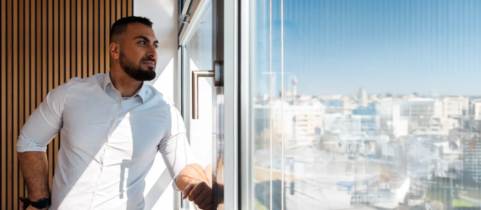 Confident business professional looking out of a modern office window with a cityscape view, symbolizing strategic thinking, leadership, and digital transformation.