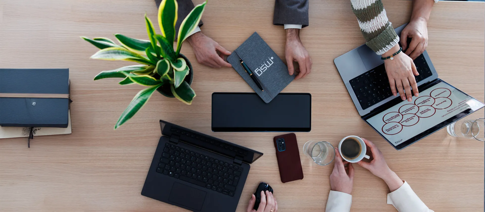 Top view of a collaborative business meeting with laptops, notebooks, coffee, and digital strategy tools, illustrating teamwork and planning in a consulting environment.