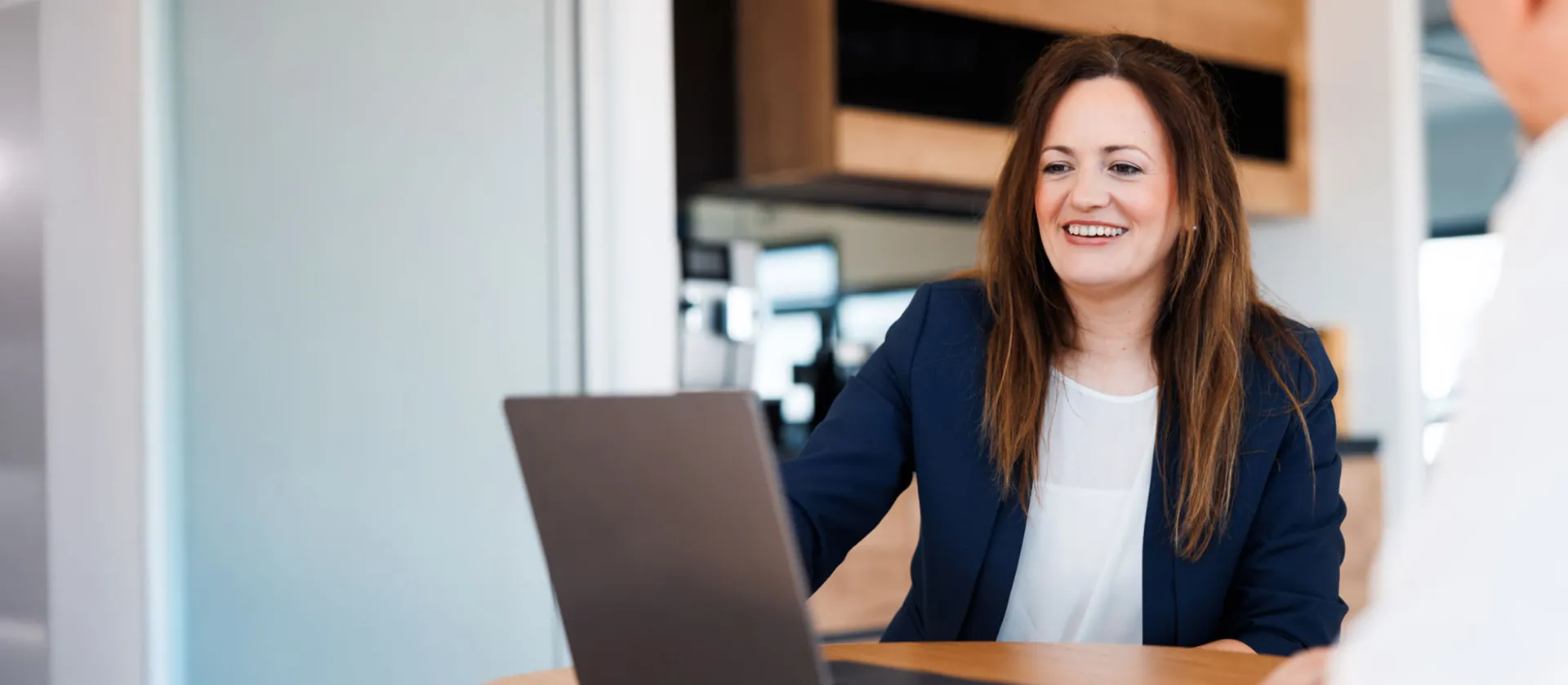 Smiling businesswoman in a blue blazer during a meeting at msg Plaut, discussing innovative digital transformation strategies with a colleague.