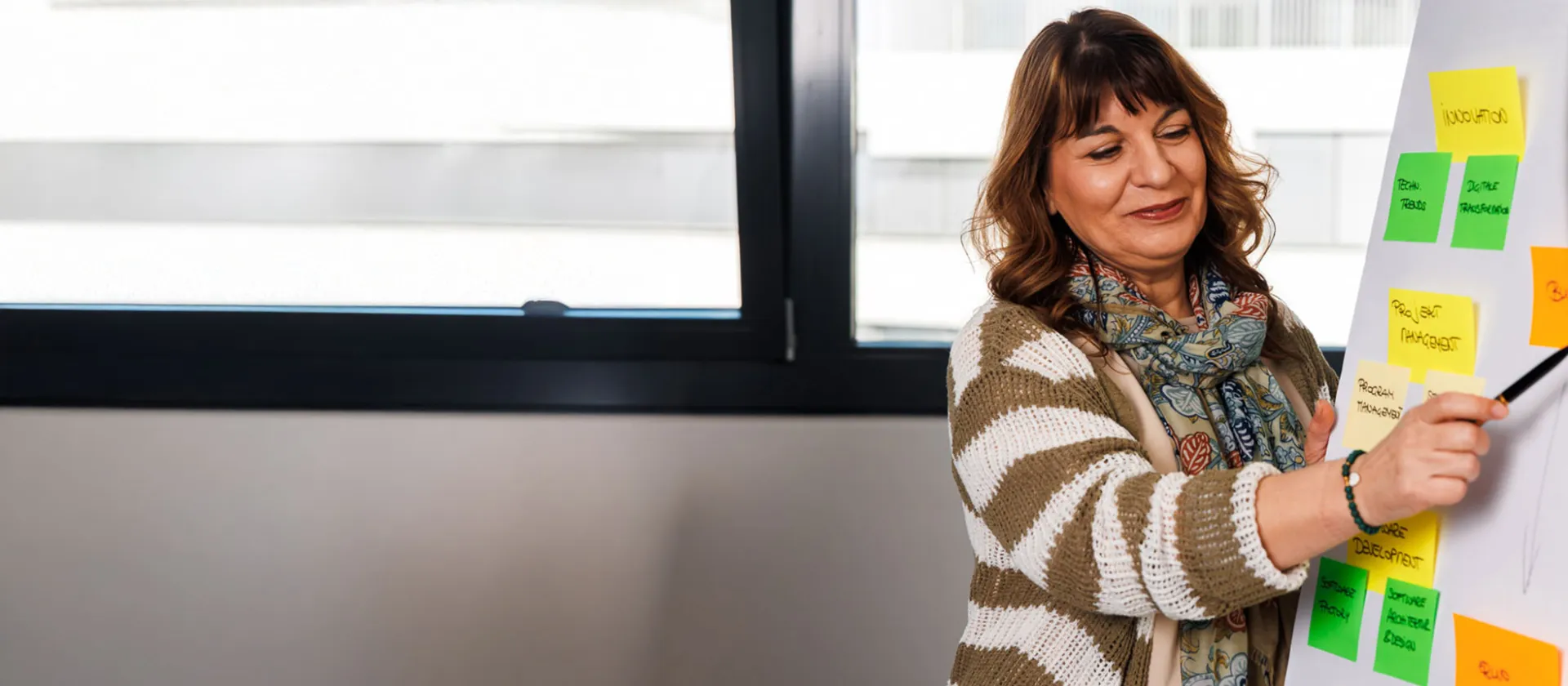 Smiling businesswoman presenting project strategy on a flip chart with colorful sticky notes in a modern office setting.