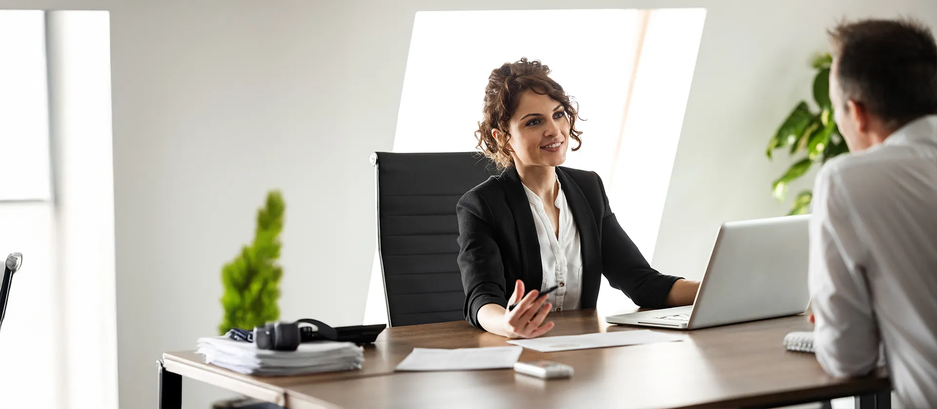 Smiling businesswoman in a modern office engaging in a professional conversation, symbolizing consulting, HR advisory, or a career interview setting.