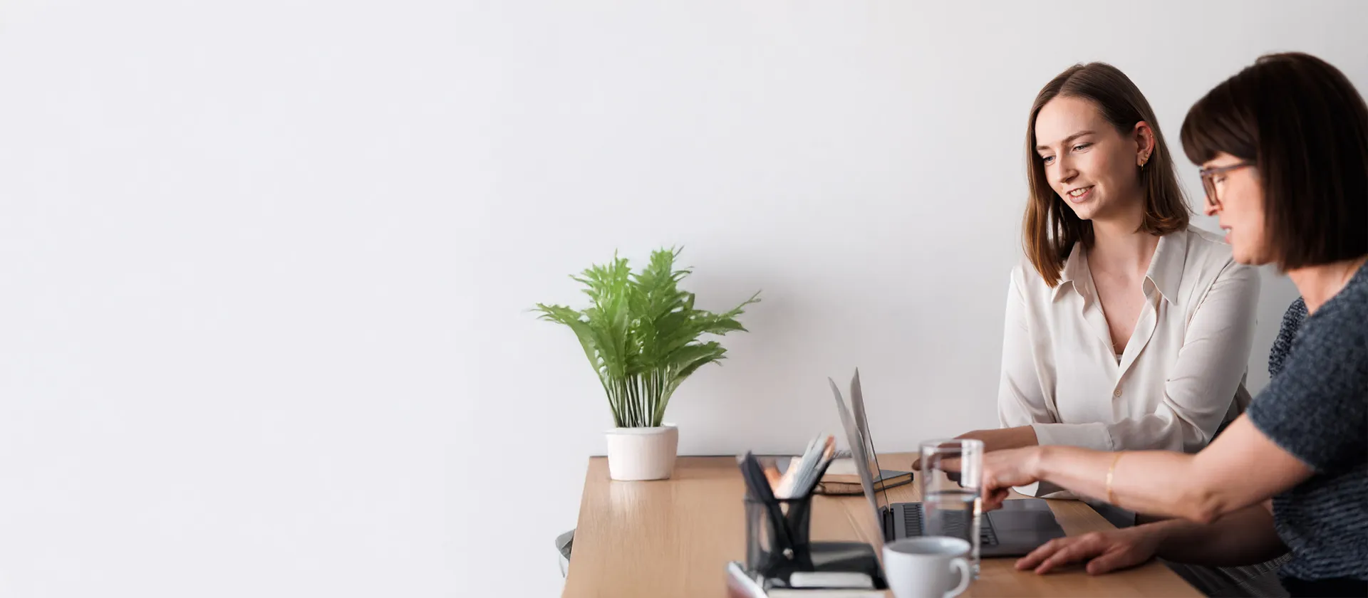 Two female professionals collaborating at a laptop in a modern, minimalistic office, symbolizing digital teamwork and SAP-driven business processes.