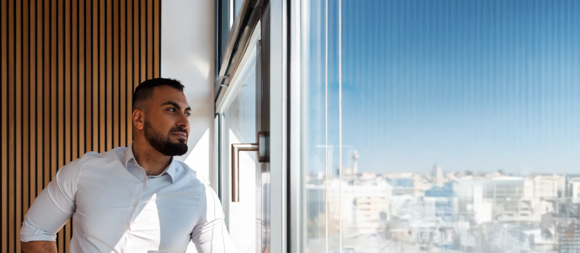 Confident business professional looking out of a modern office window with a cityscape view, symbolizing strategic thinking, leadership, and digital transformation.