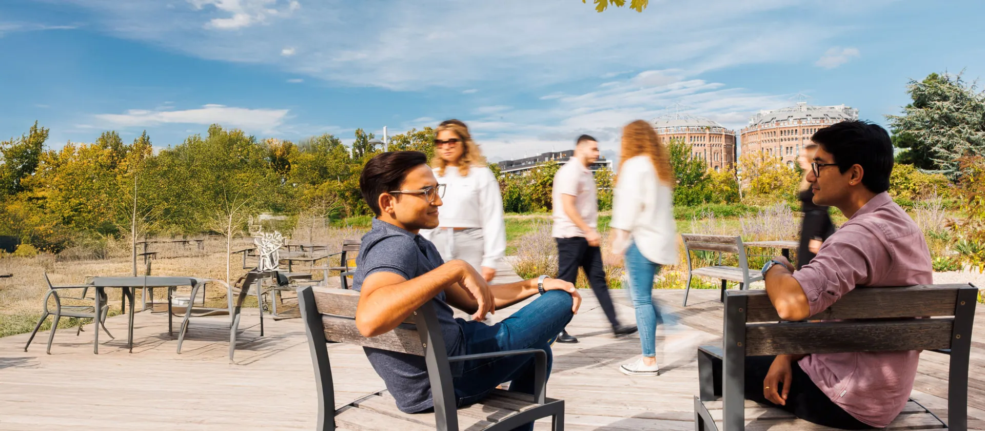 Two colleagues from msg Plaut engaging in a relaxed outdoor discussion on a sunny day, with modern architecture and greenery in the background.