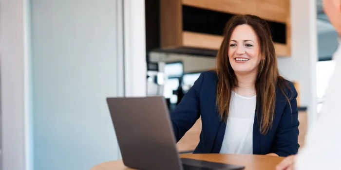 Smiling businesswoman in a blue blazer during a meeting at msg Plaut, discussing innovative digital transformation strategies with a colleague.