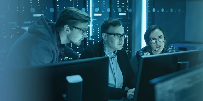 Zwei Kollegen und eine Kollegin aus dem Bereich Cyber Security sitzen konzentriert an einem Arbeitsplatz, von blauem Gradient überlagert