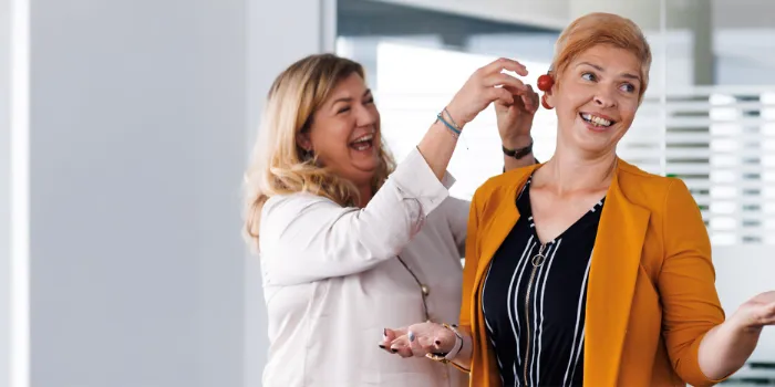 Two female colleagues at msg Plaut sharing a playful moment in the office, symbolizing a positive work culture and strong team spirit.