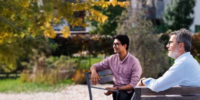 Two professionals sitting on a park bench, engaged in an informal outdoor conversation, reflecting the company’s commitment to collaboration, innovation, and people-centric solutions.