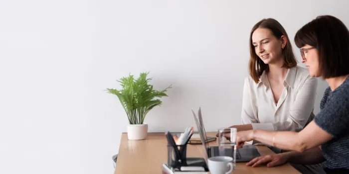 Two female professionals collaborating at a laptop in a modern, minimalistic office, symbolizing digital teamwork and SAP-driven business processes.