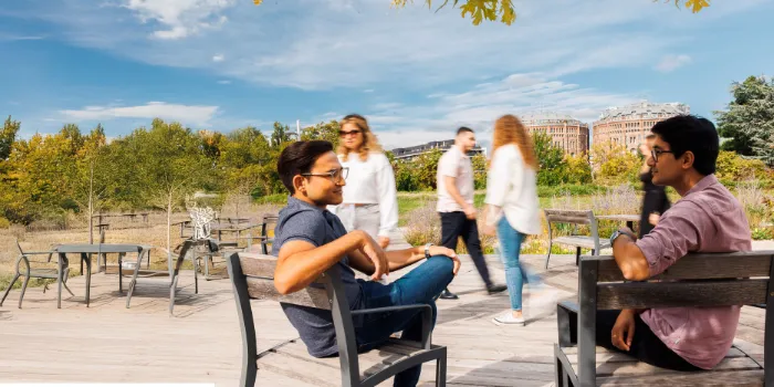 Two colleagues from msg Plaut engaging in a relaxed outdoor discussion on a sunny day, with modern architecture and greenery in the background.