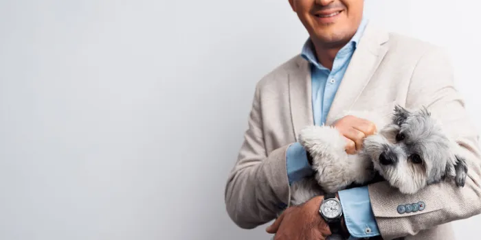 Business professional in a beige suit holding a small grey dog, reflecting msg plaut’s people-first culture and innovative approach to consulting and technology solutions.