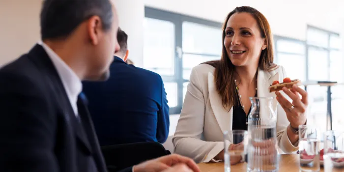 Smiling businesswoman in a white blazer engaging in conversation during an informal company lunch meeting, highlighting a positive and collaborative workplace atmosphere.