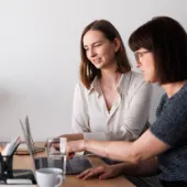 Two female professionals collaborating at a laptop in a modern, minimalistic office, symbolizing digital teamwork and SAP-driven business processes.