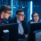 Zwei Kollegen und eine Kollegin aus dem Bereich Cyber Security sitzen konzentriert an einem Arbeitsplatz vor ihren Rechnern