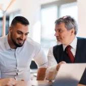 Three professionals in a collaborative discussion around a laptop in a bright office setting, symbolizing teamwork, consulting, and digital transformation planning.
