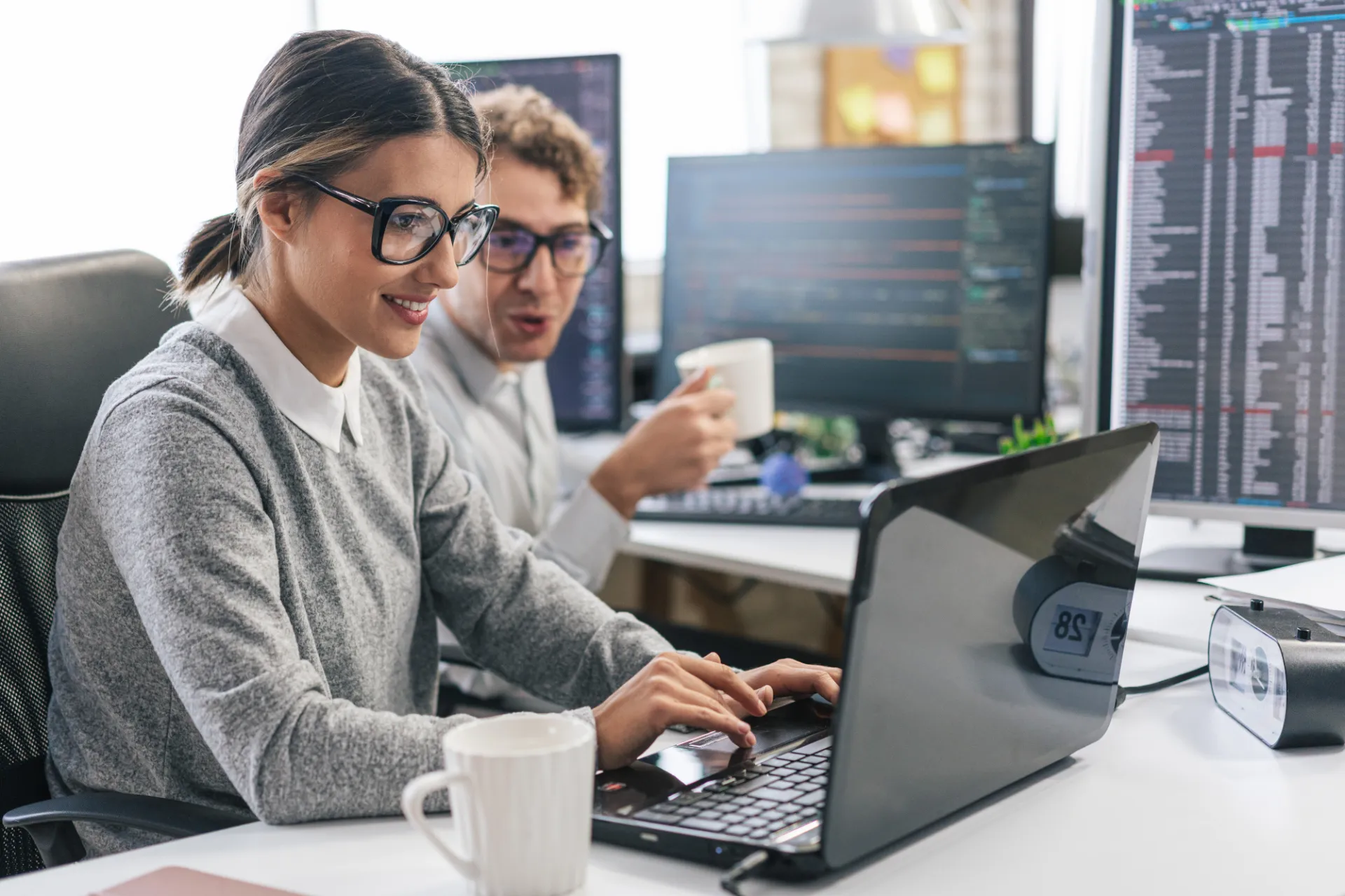 Eine Mitarbeiterin tippt auf ihrem Laptop während ein Kollege sich zu ihr dreht und etwas einwirft