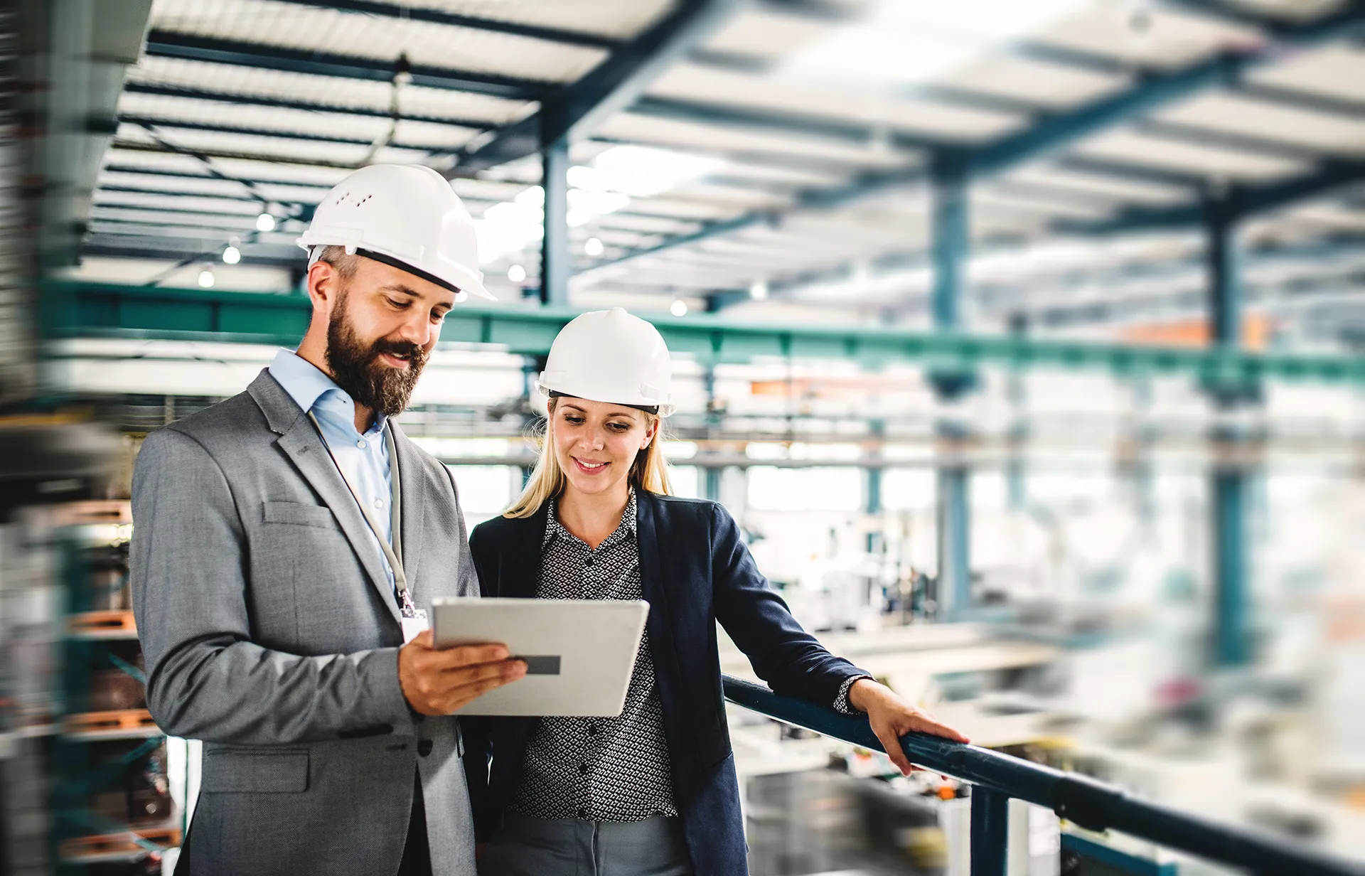 Two business professionals in safety helmets reviewing digital data on a tablet inside a modern industrial facility, symbolizing msg Plaut’s expertise in digital transformation and smart manufacturing solutions.