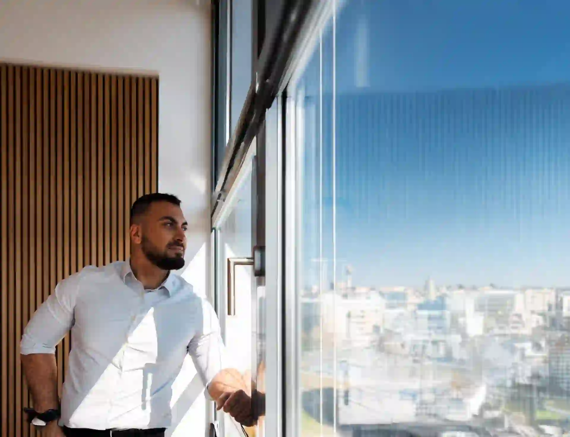 Confident business professional looking out of a modern office window with a cityscape view, symbolizing strategic thinking, leadership, and digital transformation.
